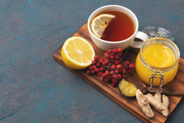 components of alternative medicine recipe how to increase immunity in self-isolation period during coronavirus pandemic. Cup of a hot tea with lemon, rowanberry, ginger and honey in a wooden spoon.