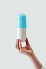 Female hand holding a large plastic blue with white pill vertically against light background