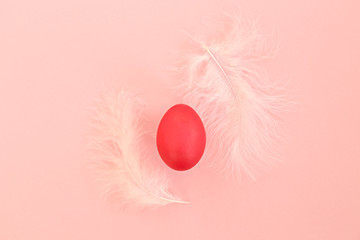 Easter egg with bunch of white feathers as decoration on pastel pink paper textured background with a lot of copy space for text. Flat lay, top view.