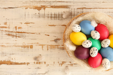 Beautiful easter table composition. Pile of painted eggs of different colors in wicker basket on grunged wood textured table background. Greeting card template. Copy space, close up, top view.