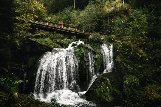 Triberger Wasserfall mit einer Br&uuml;cke und Person in roter Jacke oberhalb des Wasserfalls.