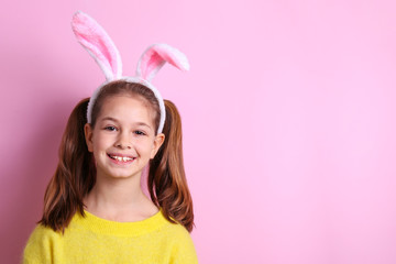 Obraz na płótnie Canvas Studio portrait of smiling young girl wearing traditional bunny ears headband for easter. Portrait of brunette female with pigtails in blank yellow sweatshirt. Pink background, close up, copy space.