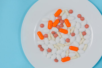 Fototapeta na wymiar Multi-colored pills in a white plate on a blue background
