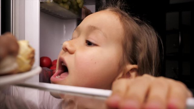 Little girl opening fridge and eating chocolate eclair at night and mom getting angry with daughter but then eating pastry too