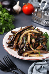 Fried eggplants with garlic and soy sauce, sliced in stripes, in a plate on a dark background, Vegetarian menu, Vertical orientation