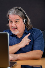 Serious business man working on laptop at his desk. He is in his 50s. He is wearing a t-shirt and a...