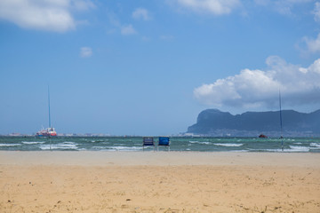 landscape of a golden sand beach, blue sky with bkanca clouds, on the shore there are two empty hammocks and fishing rods, boats in the sea and in the background we see the rock of Gibraltar