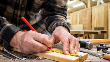 Close-up. Carpenter with pencil and the meter marks the measurement on a wooden board. Construction...