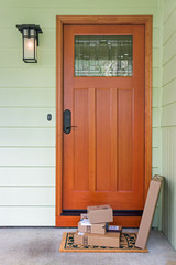 Recently delivered packages sit on a welcome mat in front of a wooden door to a residence.