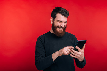 Photo of happy man surfing on internet with tablet standing over red background