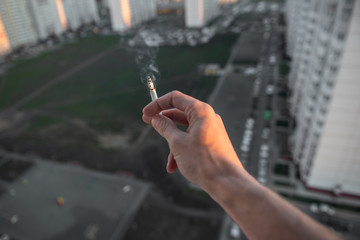 A man smokes on the balcony of a multi-storey building against the backdrop of the city. Smoking ban
