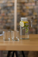 A jug of lemonade with a sprig of mint stands on a wooden table next to the glasses.