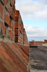 a wall of red brick goes into the distance against the sky with clouds