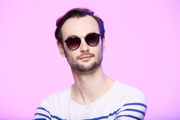 Studio shot of handsome man wearing sunglasses over pink background.