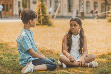 Fototapeta premium Cheerful Boy And Girl Sits On Meadow Looking Each Other