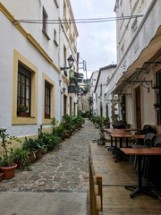 Fototapeta na wymiar Historic, narrow spanish street with a restaurant terrace, guesthouse, flowers, and a street lamp