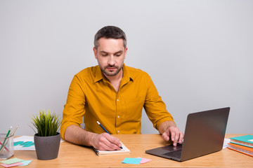 Portrait of focused mature man marketer work home computer write copybook plan wear yellow fashion shirt sit desk isolated over grey color background