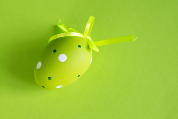 Decorative green egg with a green satin ribbon on a green background. Easter concept.