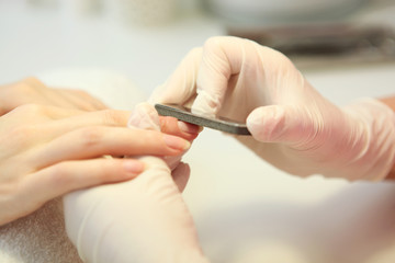 Closeup shot of a woman in a nail salon getting a manicure by a cosmetologist with a nail file. Woman gets a manicure of nails. Beautician puts nails on the client.
