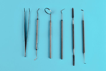 Set of metal dentist tools and equipment isolated on a blue background. Steel made mouth mirror, periodontal explorer scaler, tweezers and other instruments. Dental health and teeth care concept