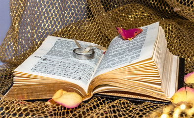 old church hymn book with wedding ring and rose petals and golden fabric as decoration.