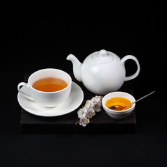 White porcelain tea set and a blooming cherry branch on a black background