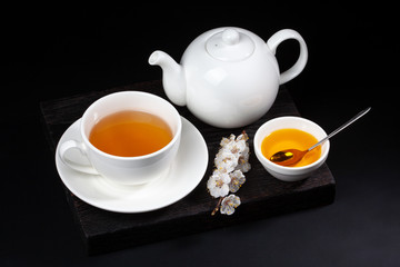 White porcelain tea set and a blooming cherry branch on a black background