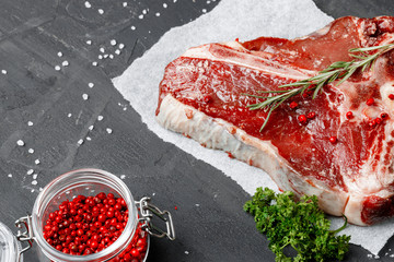 Raw fresh meat t-bone steak with spices on a dark background, close up