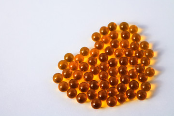 Yellow capsules of vitamins lie on a table on a white background in the shape of a heart
