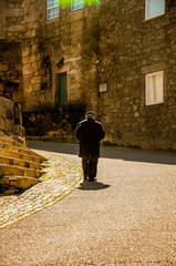 Elderly man, old man, walks alone, cold, on his back, in a medieval stone village, in winter, in the mountains, Monsanto, Portugal