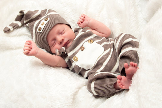 Portrait of a sleeping baby boy in a striped suit and hat on a white blanket in the studio.