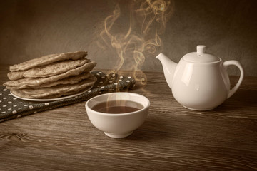 A bowl filled with hot tea next to a teapot and a green napkin on which is a plate with traditional empanadas. Vintage photo