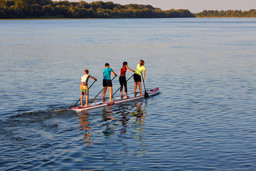 Four teenagers row on a large stand up paddle board on the Danube river at summer