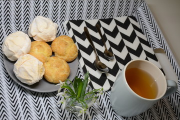 Morning breakfast. Tea and plate with eclairs and marshmallows. Pattern in white-black arrow. Vase with snowdrops