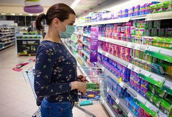 Woman wearing disposable protective face mask shopping in supermarket during coronavirus pneumonia outbreak and lockdown. Coronavirus contagion prevention measures during covid-19 pandemic.