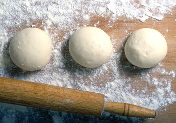 Several balls of dough and rolling pin on a wooden board