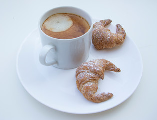 A cup of coffee with two croissants on a white table.