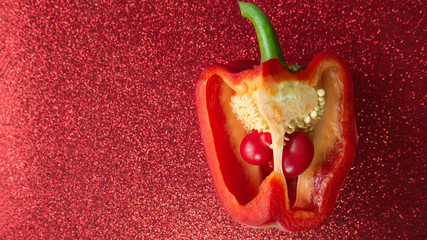 Two small bell peppers growing inside a red one, red glitter backdrop.