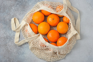 Oranges and tangerines in an eco-friendly reusable bag. The concept of dealing with garbage. View from above. Light background. Close-up.