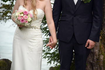 Young married couple holding hands and bouquet of flowers, ceremony wedding day, wedding rings
