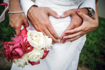 Young married couple holding hands in symbol of heart on bouquet of flowers, ceremony wedding day, wedding rings