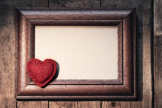 old wooden frame on a wooden wall, rustic style, textured red heart in the left corner, free space for text