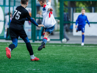 Boys in white and blue sportswear plays football on field, dribbles ball. Young soccer players with ball on green grass. Training, football, active lifestyle for kids concept