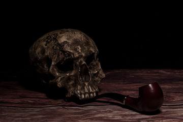 Still life with human skull, old tobacco pipe on wooden table