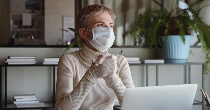 Millennial business woman wears medical face mask and gloves for coronavirus protection working from home office using laptop. Remote job, social distancing quarantine, infection spreading prevention.