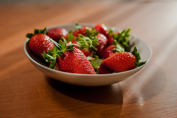 Selective focus on fresh strawberries in a bowl on wooden table. Sunny scene of fresh strawberry in a clay plate on the table.