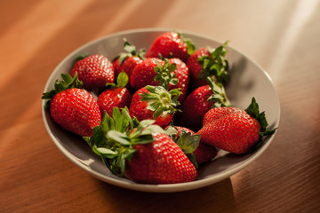 Selective focus on fresh strawberries in a bowl on wooden table. Sunny scene of fresh strawberry in a clay plate on the table.