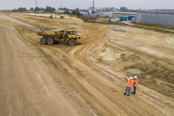 Top view of two road construction workers in orange vests and protective helmets in the middle on the field