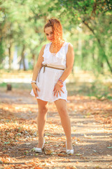 Red-haired girl in a white dress in the park in early autumn