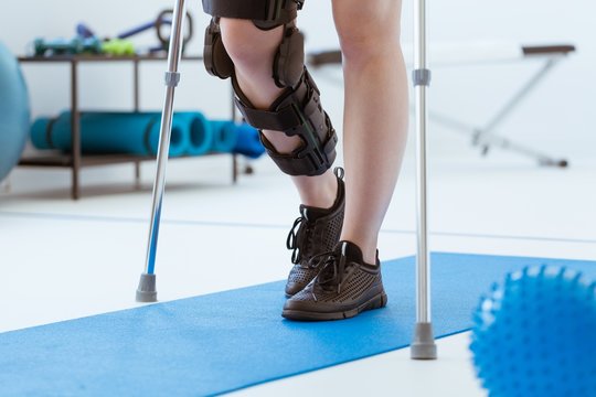 Injured patient in a leg brace exercising on a blue mat in a physiotherapy office